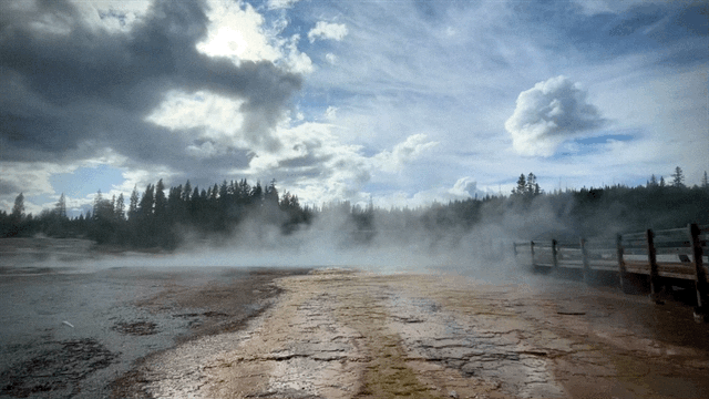 Steam rises over a hot spring runoff area with clouds in the sky above